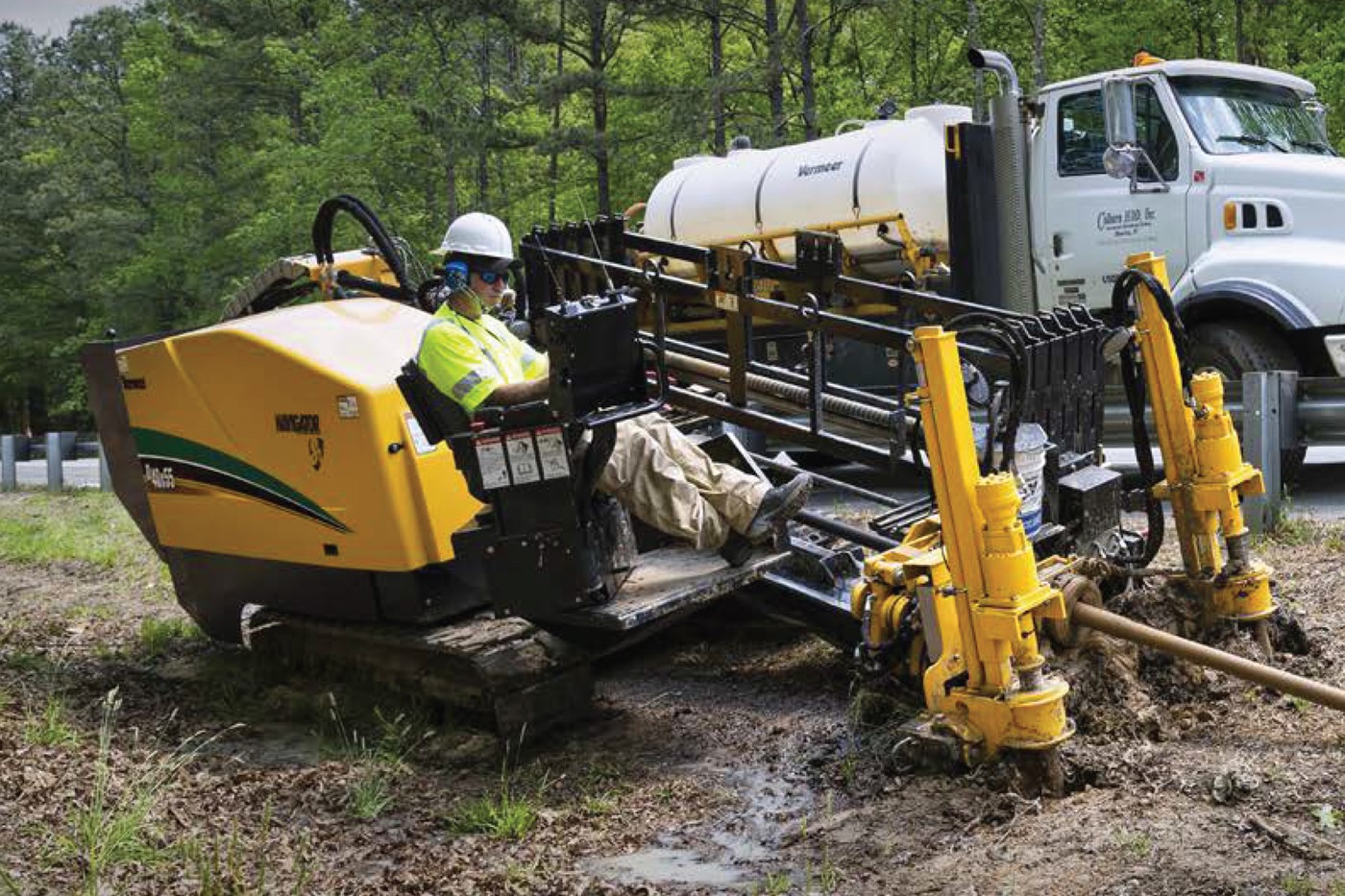Horizontal directional drilling rig working on muddy ground beside a road